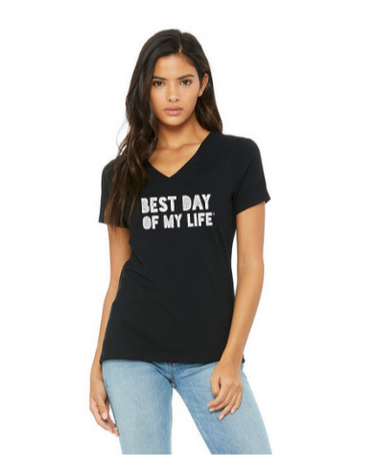 medium-skinned person with long brown hair wearing a black vneck t-shirt with best day of my life written across in white block lettering